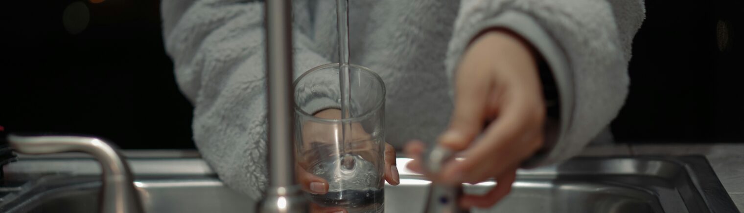Une personne remplit un verre d’eau potable à l’évier, illustrant les bienfaits de l’osmose inversée contre les PFAS.
