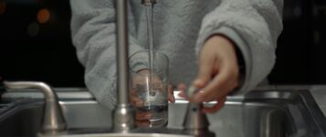 Une personne remplit un verre d’eau potable à l’évier, illustrant les bienfaits de l’osmose inversée contre les PFAS.